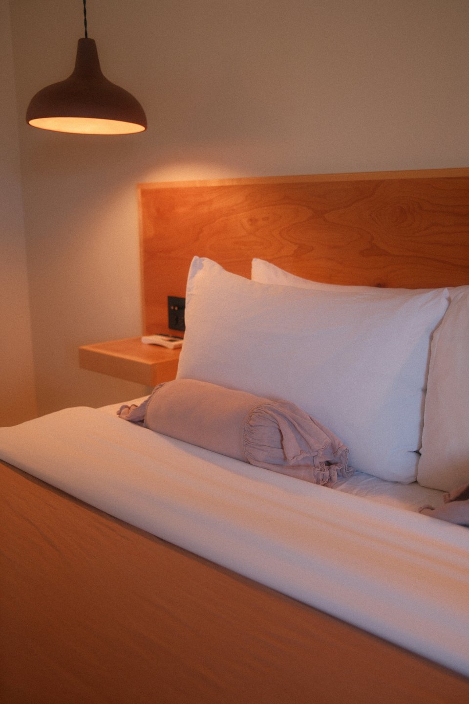 Letto moderno con cuscini bianchi e un cuscino a rotolo rosa.